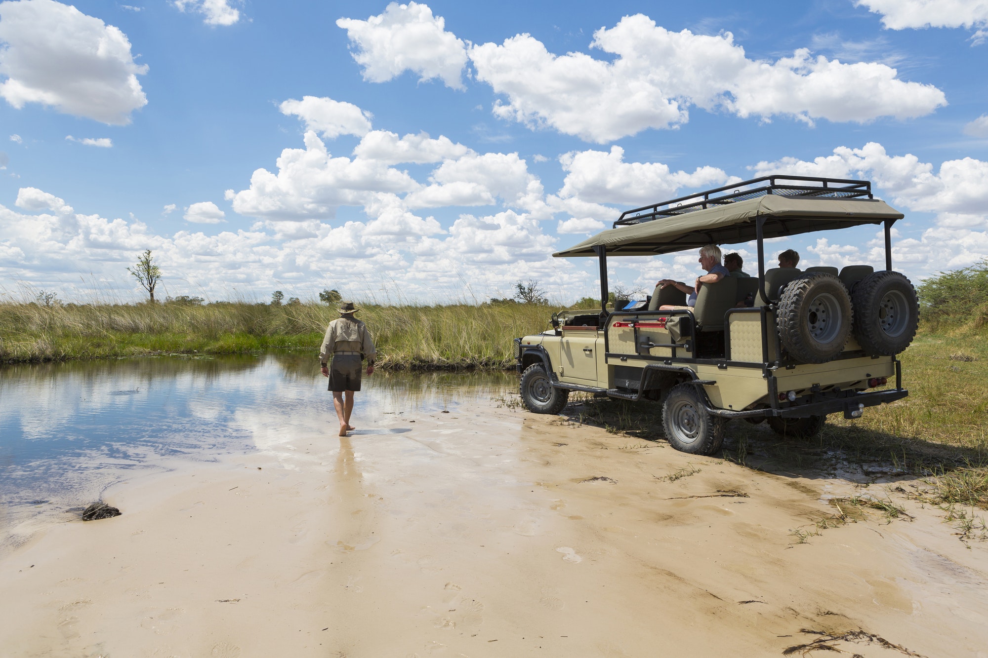 A safari vehicle with passengers, and a guide walking across sand